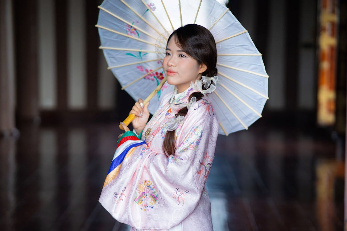 Young woman in traditional dress holding a paper parasol, illustrating umbrellas’ ancient origins.