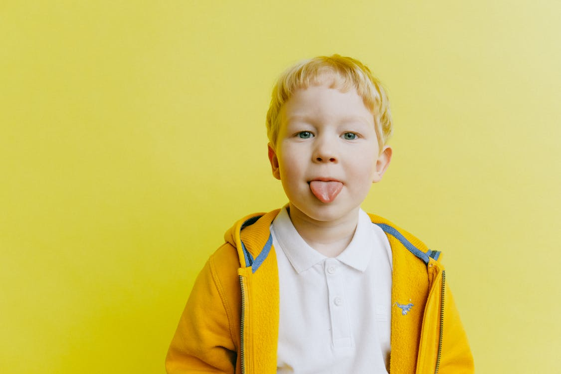 Playful kid sticking out tongue against a bright yellow background