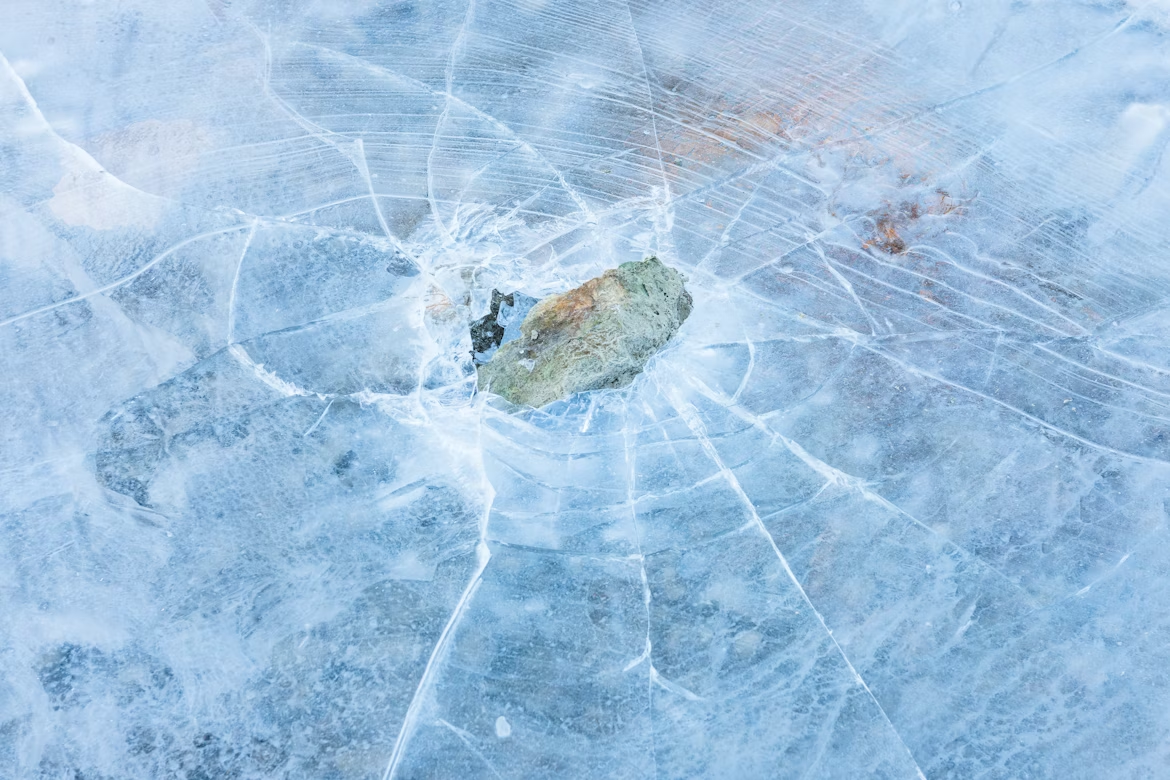 Close-up of a rock embedded in cracked blue ice, a literal “break the ice” concept