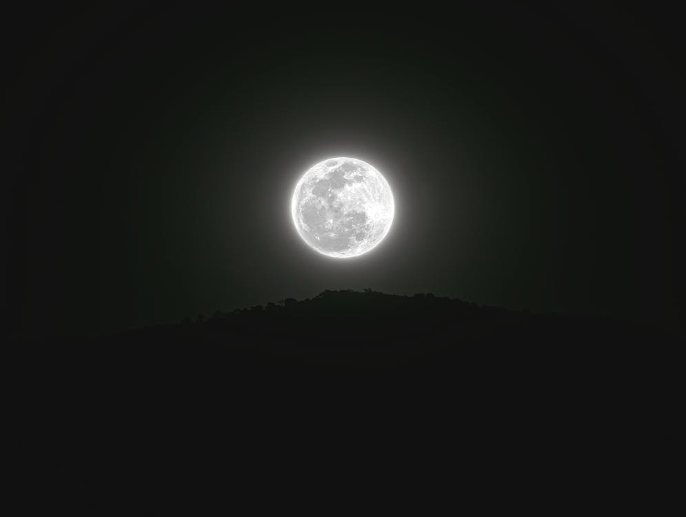 Full moon rising above a dark hillside, symbolizing objects older than Earth’s mountains.